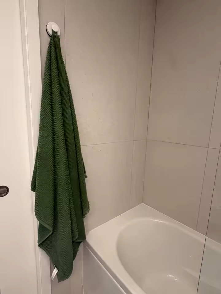 Suction hook holding a large green towel next to a bathtub